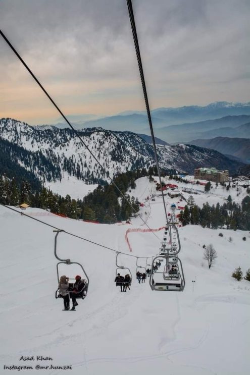 Families enjoying a chair lift ride in snowy mountains of northern Pakistan during a winter vacation
